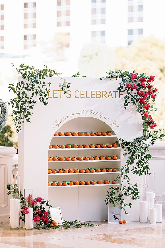 Wedding seating chart with escort card display board, greenery garland and pink flowers, citrus accents and candles on an outdoor terrace