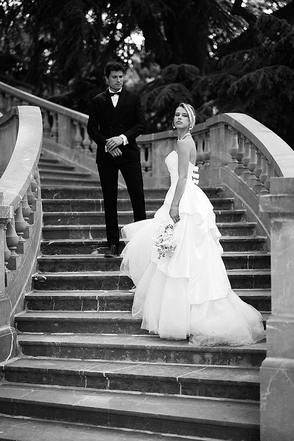 Couple portrait in a black and white wedding portrait on a stone staircase, bride in strapless tulle gown holding bouquet, groom in tuxedo behind