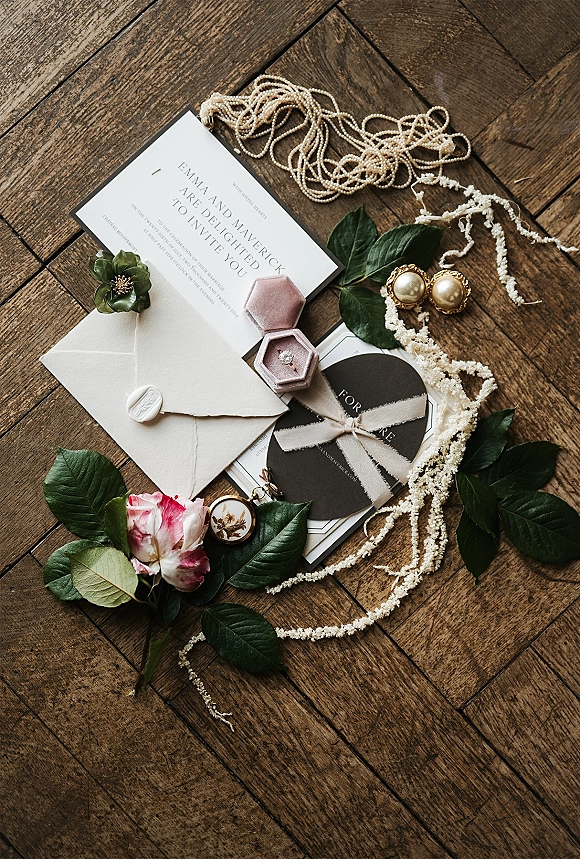 Invitation suite wedding invitation flat lay with deckle edge envelope, wax seal, velvet ring box and pearls arranged on a wood parquet floor
