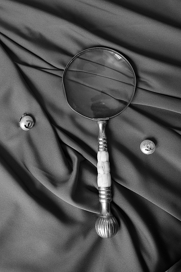 Groom accessories flatlay with cufflinks and a magnifying glass arranged on textured suit fabric and softly draped cloth background