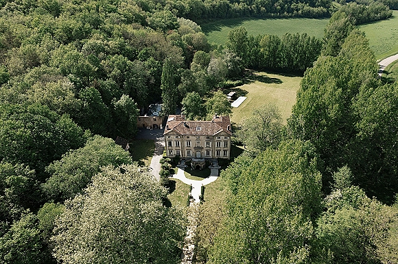 Wedding venue with a manor house and gravel driveway, framed by landscaped gardens and lawns, backed by forest and open fields