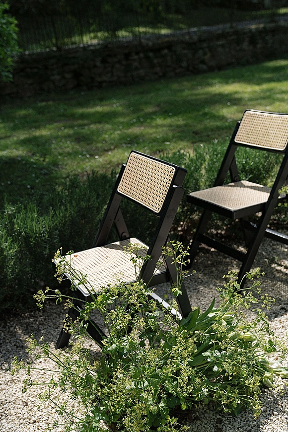 Ceremony seating with outdoor ceremony chairs featuring woven cane backs beside a gravel aisle with greenery in a garden lawn setting