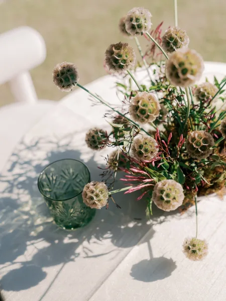 Wedding centerpiece featuring a sculptural seed pod centerpiece with organic greenery, paired with a green glass tumbler on the table.