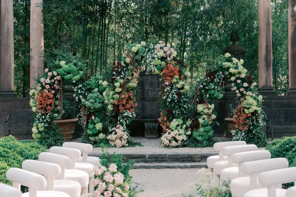 Ceremony setup framed by floral arches, lush garden ceremony decor in a bamboo garden with stone columns and a gravel aisle.