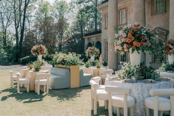 Outdoor reception decor in a garden reception setup, featuring tall centerpieces on round tables set on a lawn before a columned mansion.