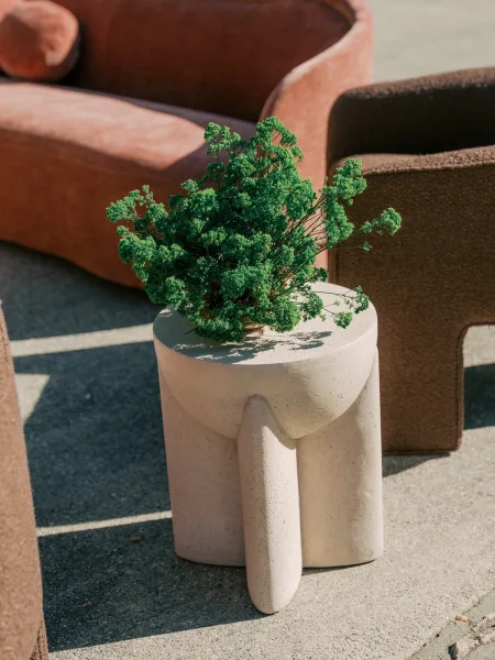 Wedding lounge decor with cozy reception lounge seating around a sculptural side table on a sunlit concrete patio with soft shadows.