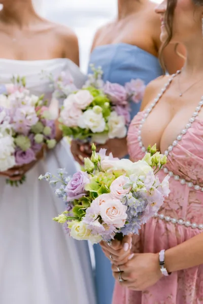 Bridesmaid bouquets of pastel bridesmaid bouquets with roses, hydrangea, and lisianthus held by women in strapless dresses outdoors