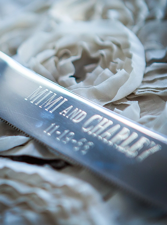 Custom wedding engraving on a personalized wedding nameplate, silver engraved metal plaque with ivory fabric flowers and ribbon on soft fabric surface