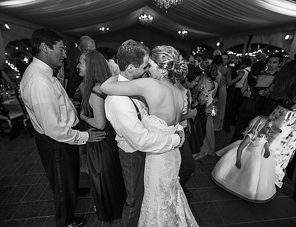 First dance as bride in a lace wedding dress hugs groom in suspenders on a reception tent dance floor under chandeliers