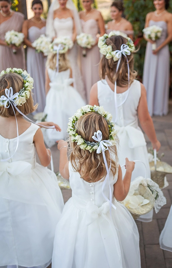 Flower girl processional with multiple flower girls walking aisle in tulle dresses and floral crowns, carrying baskets down a greenery walkway