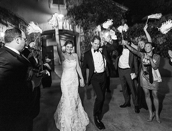 Wedding send off with bride in wedding dress and groom in tuxedo walking through sparklers on an outdoor walkway at night entrance