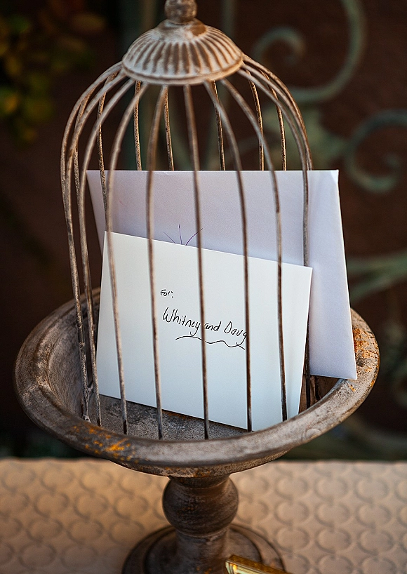 Wedding card box with birdcage card holder design, filled with calligraphy cards and envelopes on a pedestal by wrought iron railing
