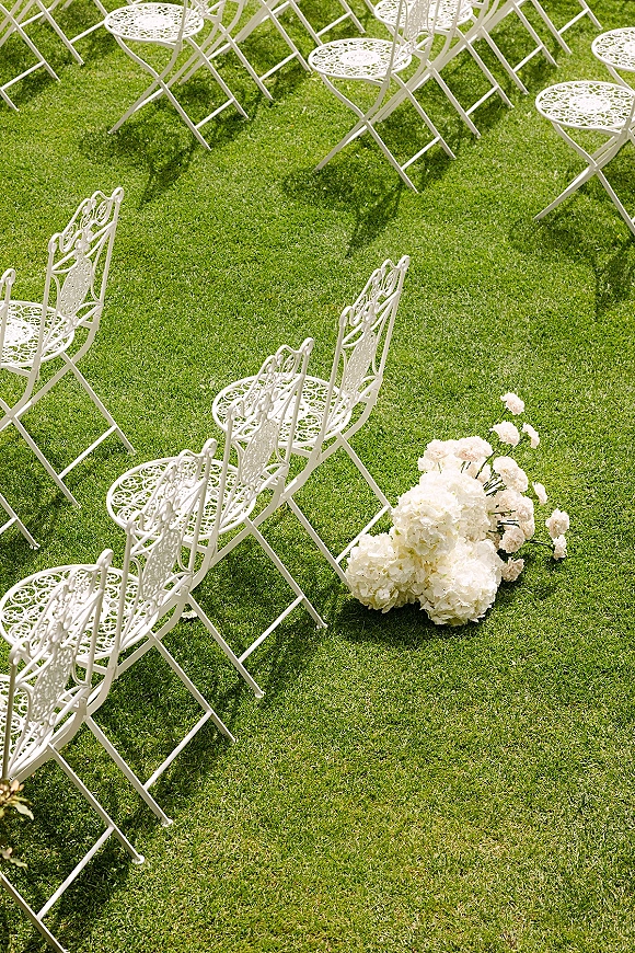 Ceremony seating with outdoor wedding chairs in neat rows on a sunlit grass lawn, accented by white flowers along the aisle