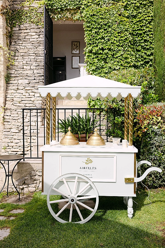 Gelato cart with scalloped canopy and gold posts, topped with domes, cups, and bowls, set on a garden patio by ivy wall