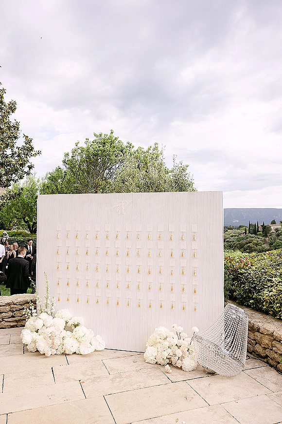 Champagne wall wedding champagne wall display with mini bottles and white floral arrangements on a stone patio with greenery and hills behind