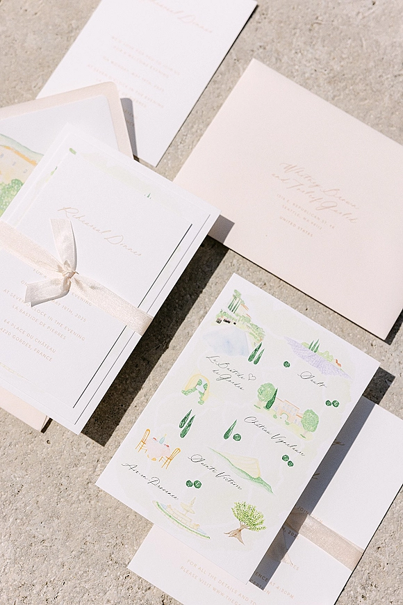 Wedding invitation suite with watercolor wedding invitations, calligraphy cards and envelope tied with a ribbon bow on sunlit stone surface
