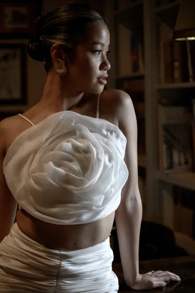 Bridal portrait of a side profile bride in a strapless satin gown with rosette bodice and statement earrings by warm window light indoors