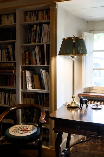 Home library corner with built-in bookshelf styling, a wooden writing desk and brass lamp beside an upholstered chair by the window