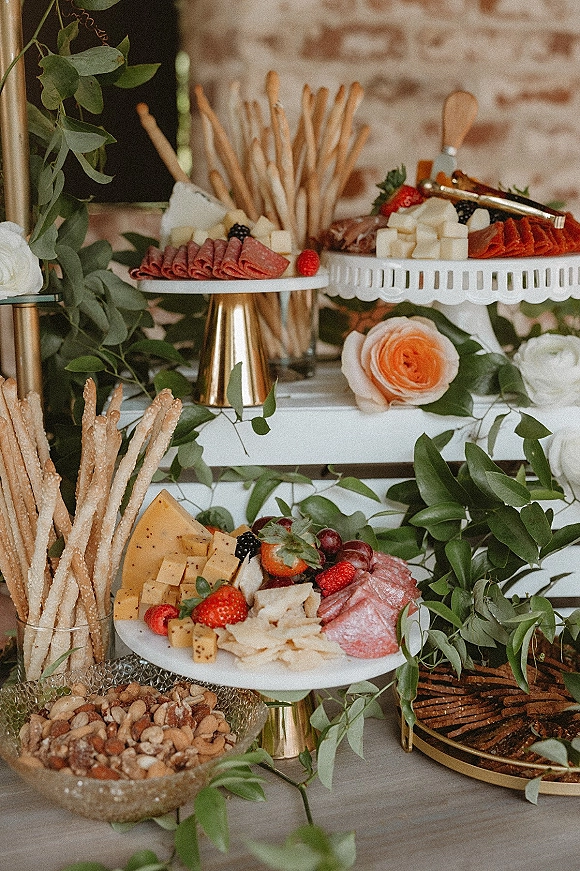 Charcuterie board wedding charcuterie table with cheese cubes, salami, fruit and crackers on tiered stands against a brick wall
