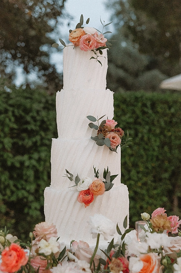 Wedding cake with textured buttercream tiers topped with roses, ranunculus, and greenery on an outdoor garden table display