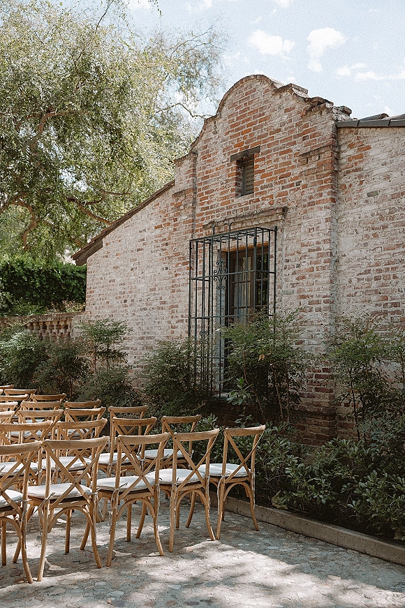Ceremony seating with outdoor wedding ceremony chairs in neat rows, wood cross back design and white cushions on a stone courtyard patio