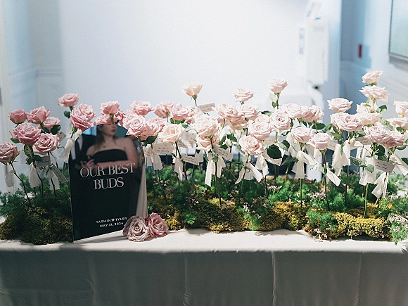 Wedding escort display with a floral escort card display of blush roses, place cards, ribbon tags, and a moss runner in window light
