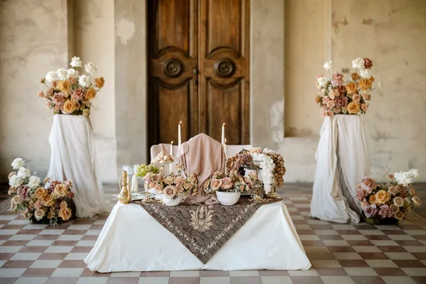 Reception tablescape with low wedding sweetheart table, patterned runner, taper candles, fruit bowls, and floral arrangements before wooden doors