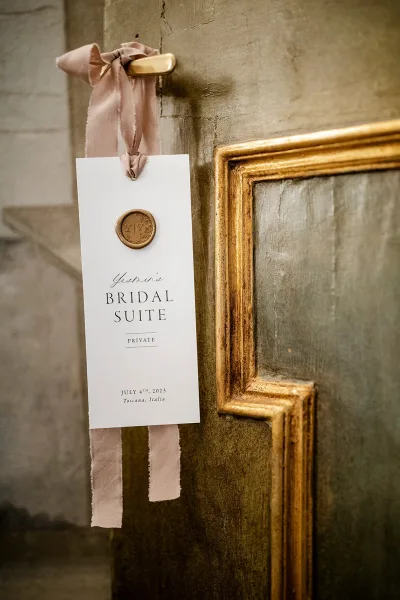 Wedding door hanger bridal suite door sign with calligraphy text, silk ribbon bow, and wax seal on a brass handle against a textured door