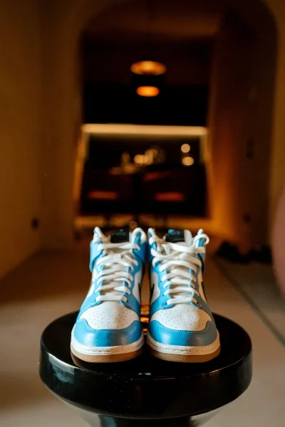 Groom shoes, blue and white wedding sneakers with white laces on a round black table in a warm, arched hallway background