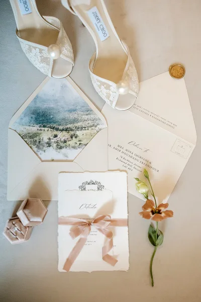 Invitation suite wedding invitation flat lay with deckled edge cards, envelopes, wax seal, silk ribbon, ring box, and pearl heels on linen