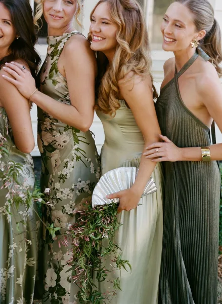 Bridesmaid portrait in sage green bridesmaid dresses, holding greenery bouquet on outdoor walkway by building steps in soft light.