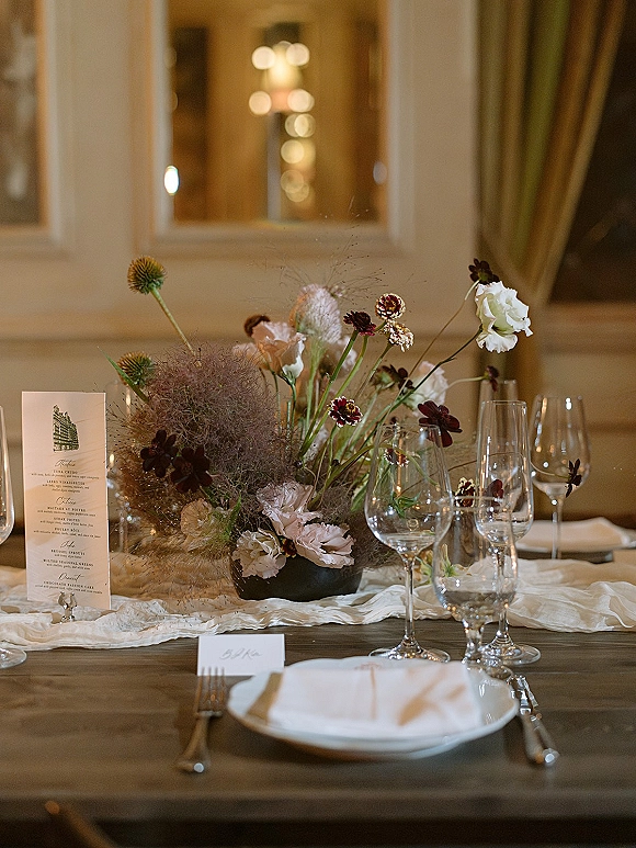 Reception tablescape with wedding table centerpiece, bud vases, menu and place cards, set on rustic wood table with warm window light