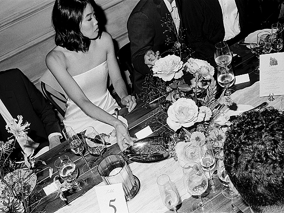 Wedding reception moment with bride in a strapless gown and groom in tuxedo seated at a wood table with rose centerpiece and candlelight