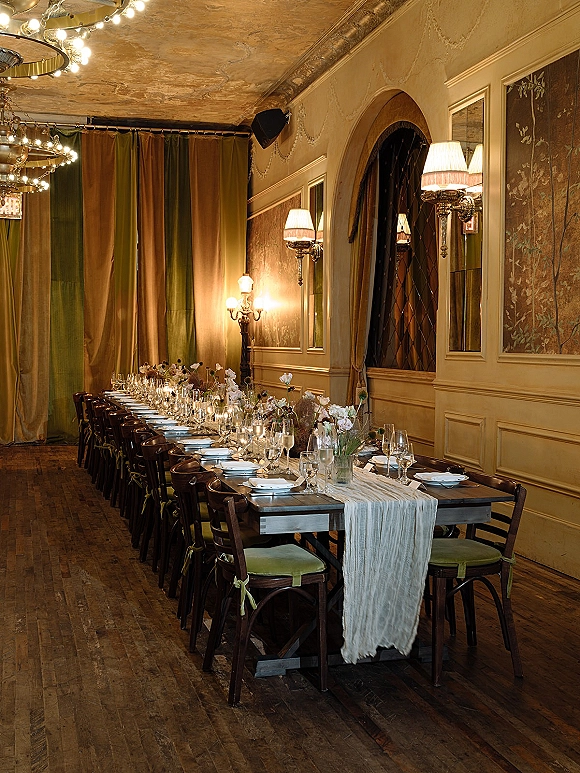 Reception tablescape with a long banquet table wedding setup, candles, floral centerpieces, and chandeliers in a vintage paneled room
