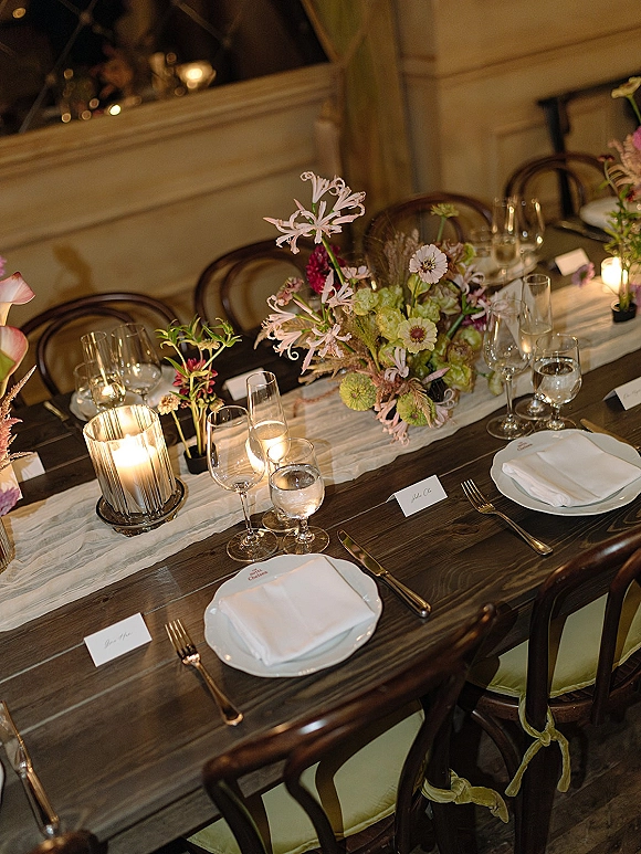 Reception tablescape with wedding head table decor featuring pastel florals, bud vases, candles, and gold flatware on a dark wood table indoors
