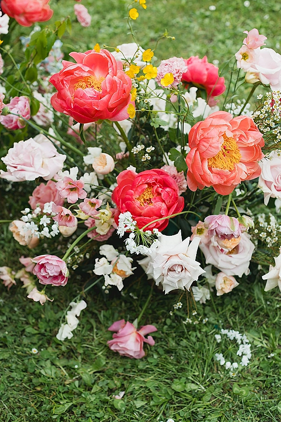 Wedding bouquet with coral peonies and white roses, blush blooms, yellow wildflowers, and greenery resting on a grass lawn