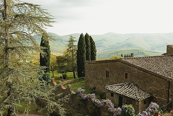 Wedding venue landscape with a stone farmhouse, terracotta roof and wisteria-covered wall, overlooking cypress-lined lawns and mountains