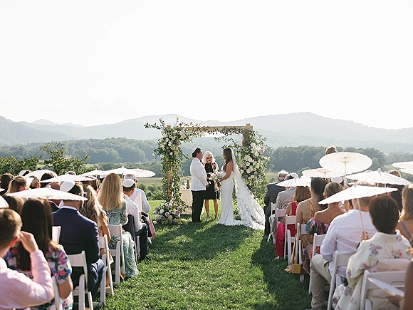 Wedding vows as the couple exchanges vows under a floral arch, bride in long veil with bouquet, mountain-view lawn ceremony setting