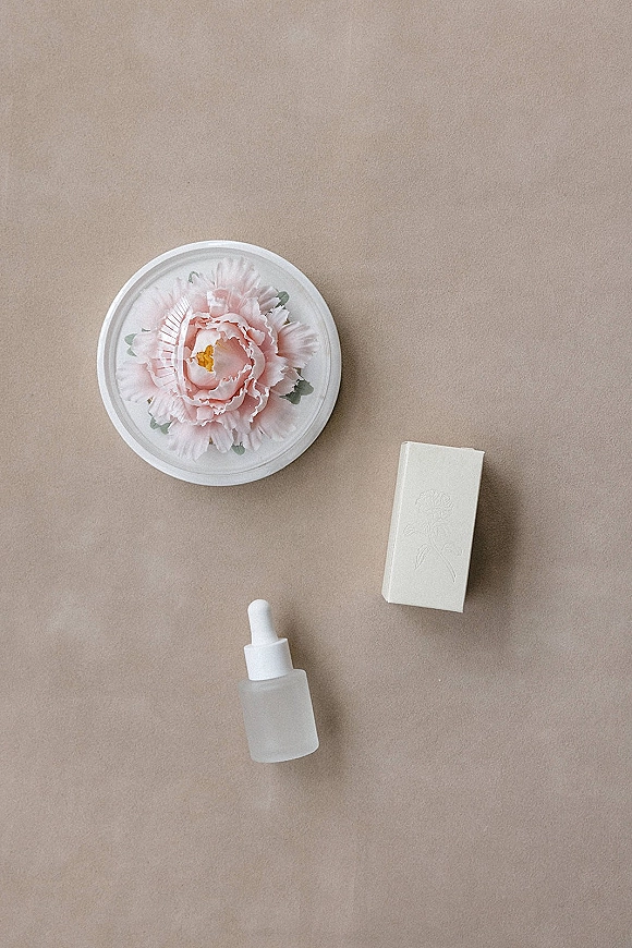 Bridal flat lay with wedding perfume flat lay details, pink peony accent, round box and white gift box on neutral fabric backdrop