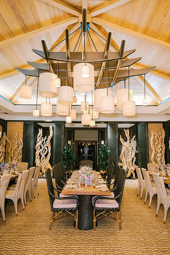 Reception tablescape with long head table decor featuring floral centerpiece runner, taper candles, and wine glasses under a vaulted wood ceiling