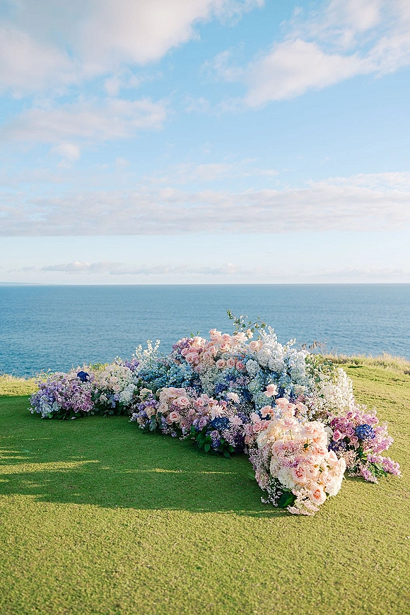 Ceremony floral arrangement on the ground floral altar with roses, hydrangea, baby's breath and greenery, set on a coastal lawn with ocean horizon