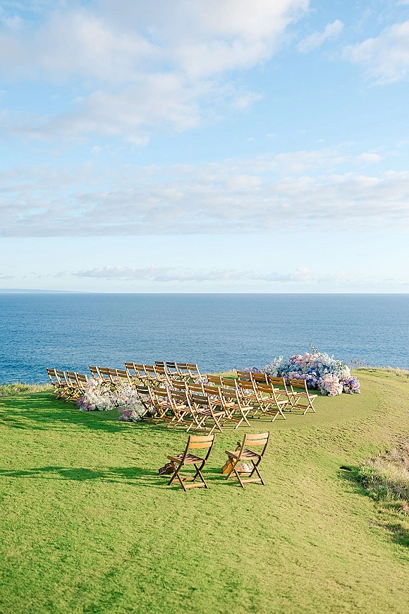 Outdoor ceremony setup with oceanfront wedding ceremony chairs in a semicircle, wood folding seats, pastel aisle florals and petals by the coast