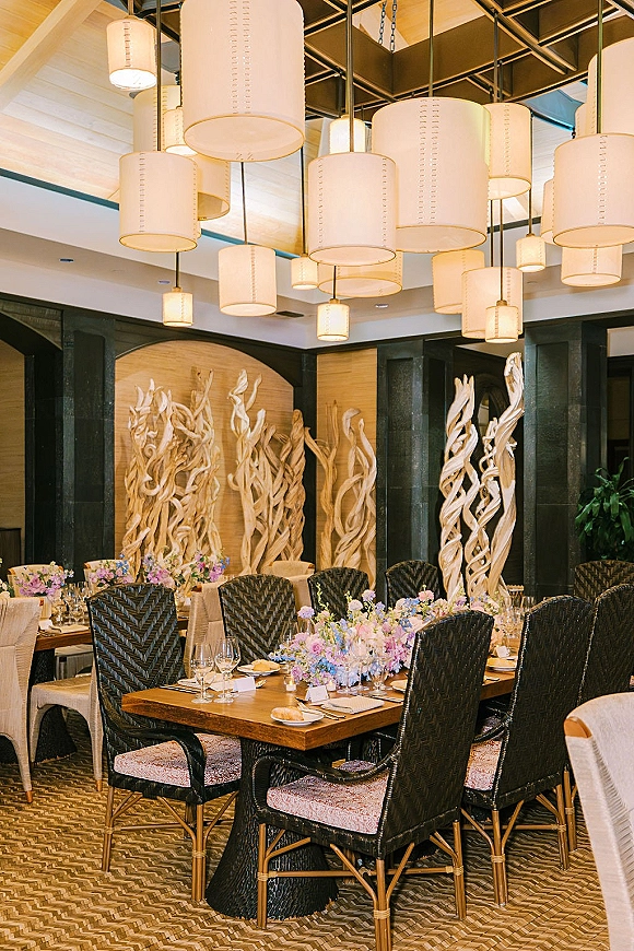 Reception tablescape with wood table wedding decor, pastel floral centerpieces, place cards, votive candles, and drum pendant lights overhead
