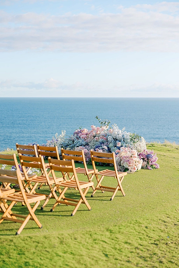 Ceremony setup with oceanfront wedding ceremony seating, wood folding chairs circling a pastel rose and hydrangea ground arch on a cliff lawn