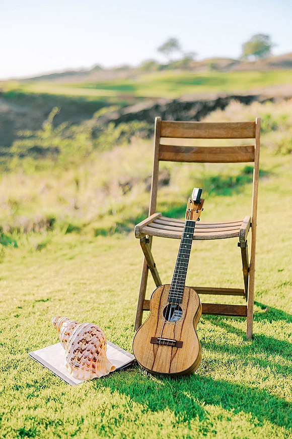 Wedding ceremony music setup with a ukulele on a wooden folding chair on a grassy lawn overlooking a hillside and open sky