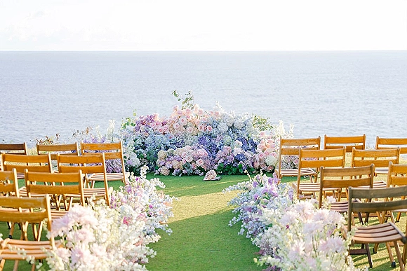 Ceremony setup with outdoor wedding ceremony aisle lined with pastel meadow flowers and wood folding chairs, set against an ocean horizon backdrop