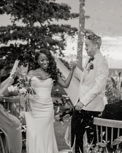 Wedding recessional with confetti wedding exit as bride in strapless dress and long veil holds bouquet, hand in hand with groom down garden aisle
