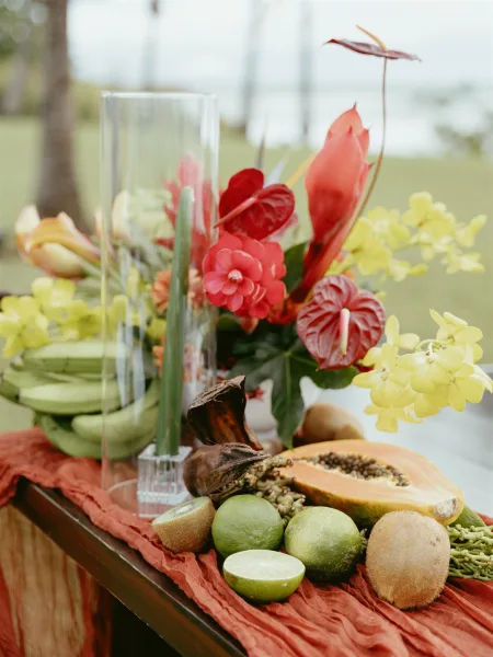 Reception centerpiece with tropical wedding centerpiece florals, anthurium and orchids in a tall hurricane vase on a wooden table by the shoreline