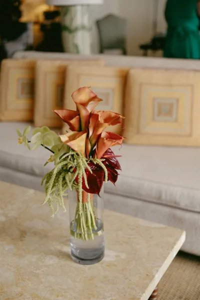 Wedding centerpiece with calla lilies in a water-filled glass cylinder vase, styled on a coffee table in an indoor lounge seating area