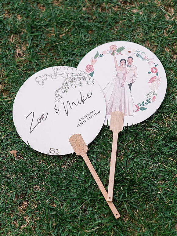 Wedding fan favors with personalized wedding fans featuring floral and couple illustrations, calligraphy names and date, on green grass lawn